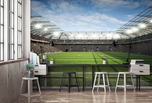 A photo wallpaper featuring a vibrant image of a football stadium with a grass field, seats, and stadium lights, installed on a wall in a room with furniture.