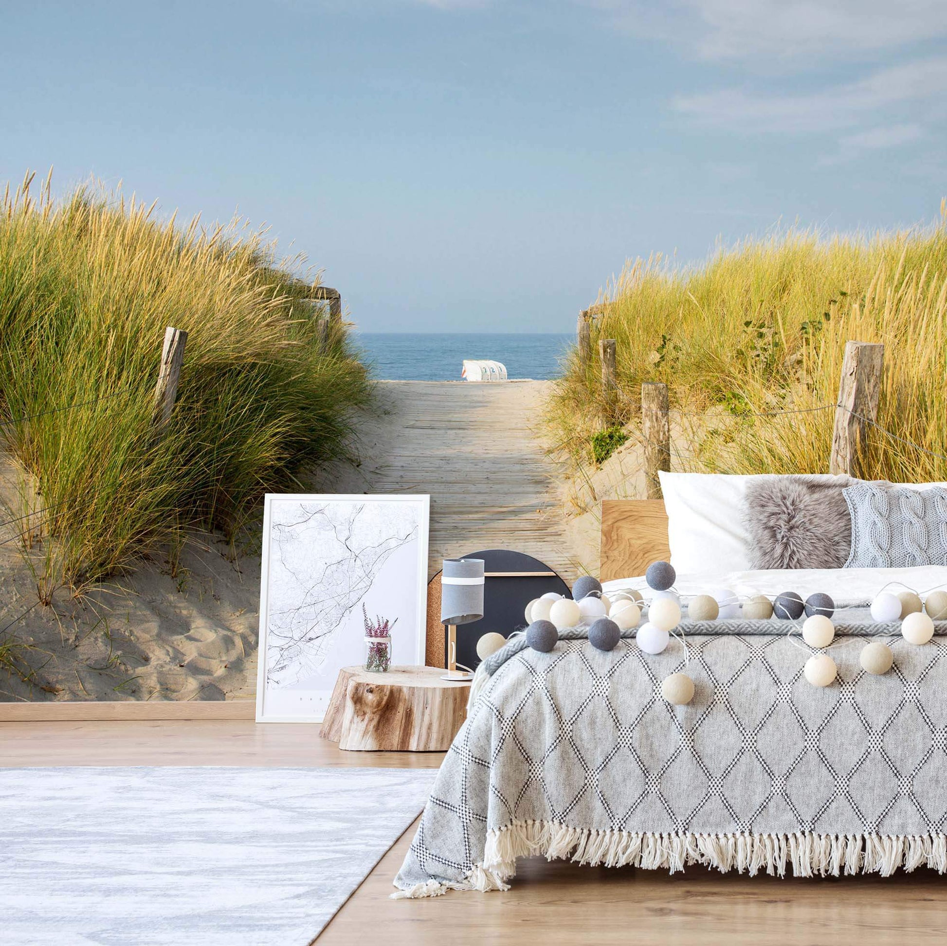 A non-woven photo wallpaper featuring a sandy beach scene with grass, displayed on a bed in a room with beach-themed decor.