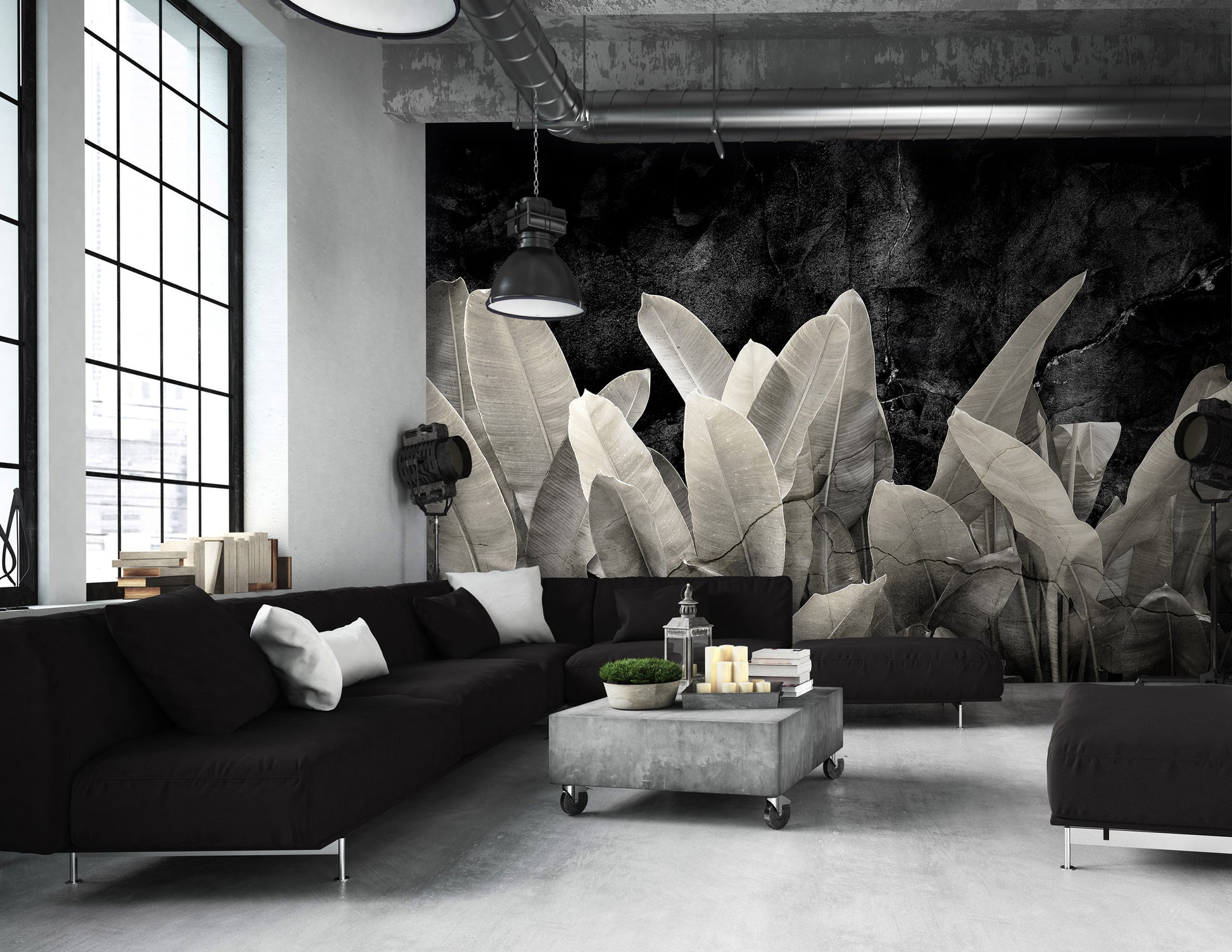 Modern living room with black sofa, gray ottoman, and large leafy plant wall mural.