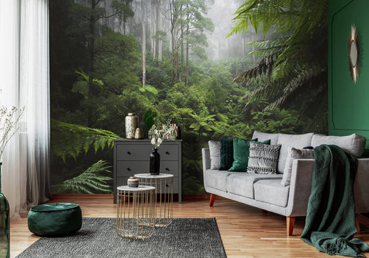 A nature-themed non-woven photo wallpaper featuring a green jungle scene, installed on the walls of a living room with a gray sofa, green accent chairs, and decorative plants.