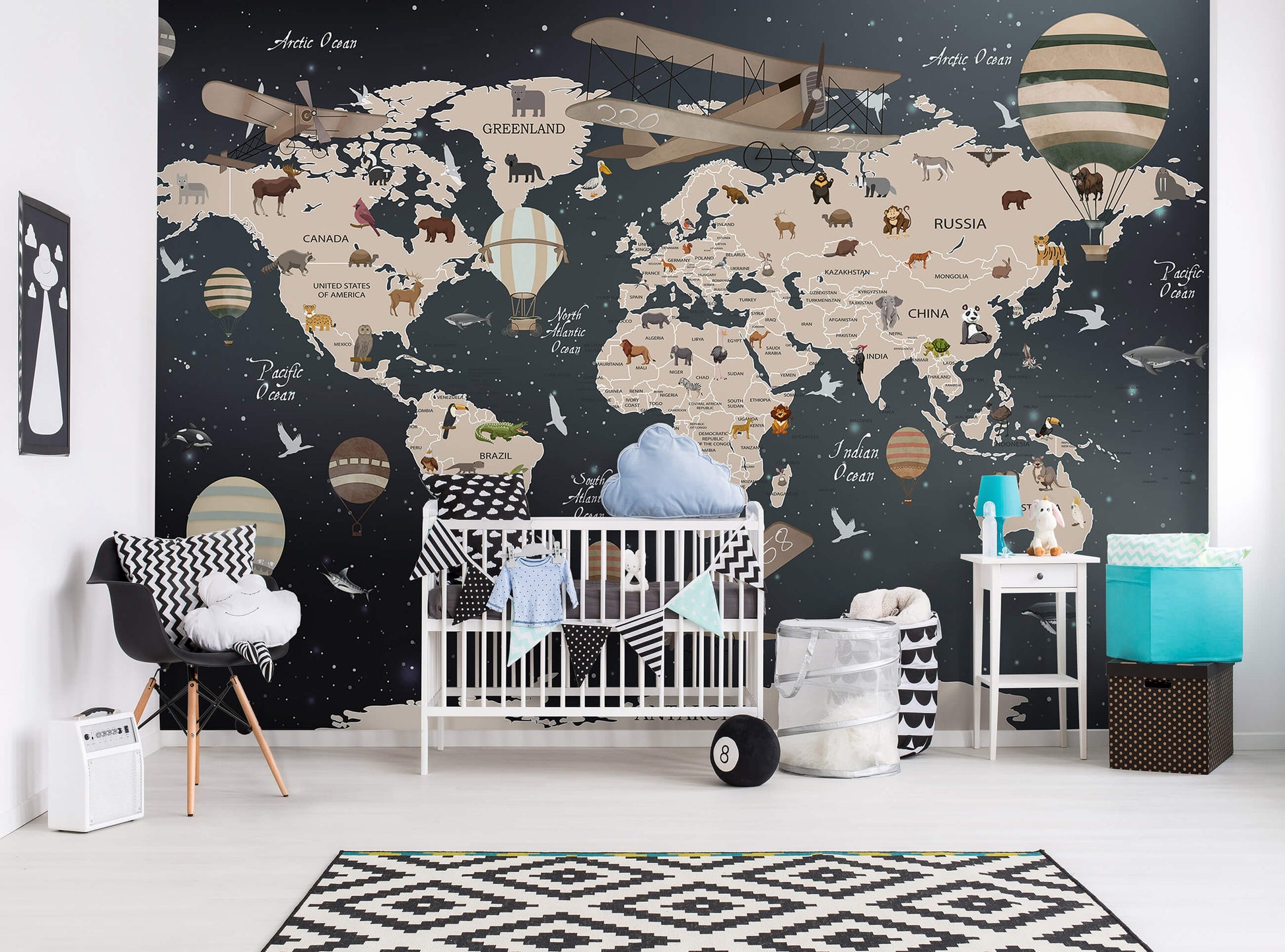 A room with black and brown non-woven photo wallpaper featuring a world map and various adventure-themed illustrations, with a crib, furniture, and decorative items.