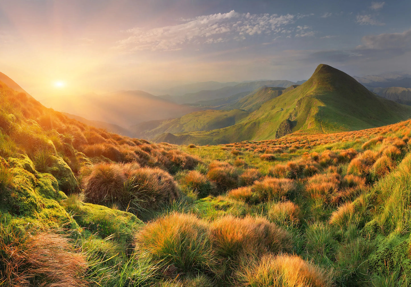 Sunrise over a mountainous landscape with green grass and clouds.