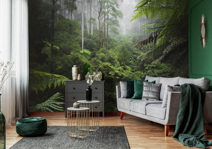 A nature-themed non-woven photo wallpaper featuring a green jungle scene, installed on the walls of a living room with a gray sofa, green accent chairs, and decorative plants.