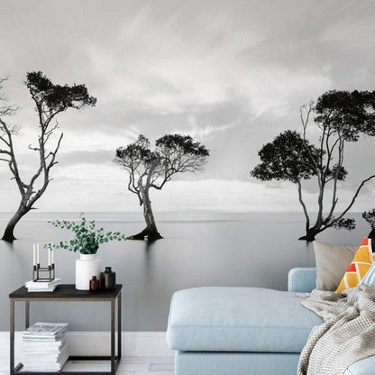 A wallpaper mural featuring trees submerged in water, with a calm lake and cloudy sky background, installed in a room with modern decor.