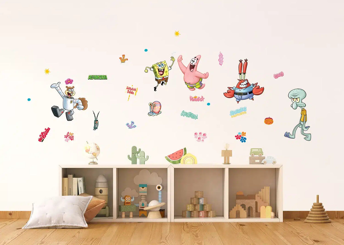 A children's room scene with SpongeBob-themed wall decals displayed on a light beige wall above a low wooden shelf with toys and books.